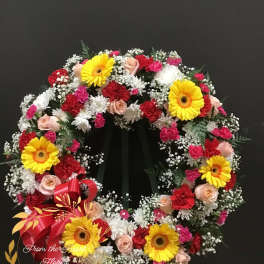 Circular floral wreath with yellow gerbera daisies, pink roses, and red carnations