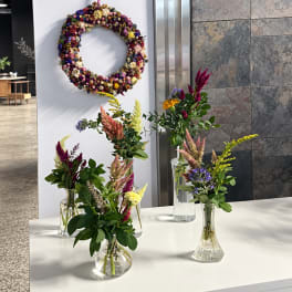 Small mixed flower arrangements in clear glass vases beside a floral wreath.
