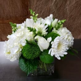 White floral arrangement in a clear square vase with green accents