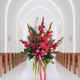 Tall pink floral arrangement with a ribbon in a church aisle