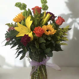 Mixed bouquet of lilies, roses, and sunflowers in a glass vase