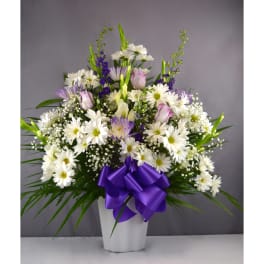 White daisies and purple flowers in a white vase with a purple ribbon
