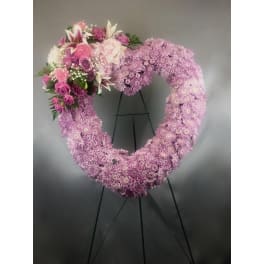 Heart-shaped pink floral wreath on a black stand