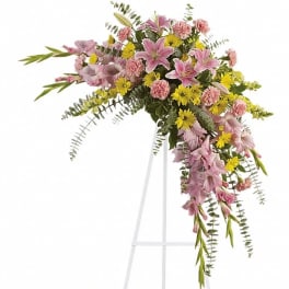 Pink lilies, carnations, and yellow daisies in a cascading spray on a white standing easel