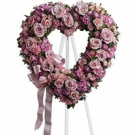 Heart-shaped floral wreath of pink and lavender roses on a stand with ribbon