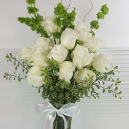 Tall arrangement of white roses and green Bells of Ireland in a clear vase with a white ribbon bow
