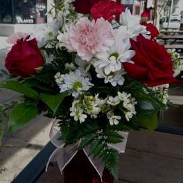 Bouquet of red roses, pink carnations, and white daisies in a red vase