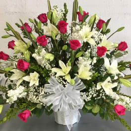 Large bouquet of pink roses and white lilies in a white vase with a sheer bow