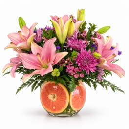 Pink lilies and purple flowers in a glass vase with grapefruit slices
