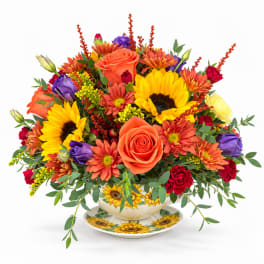 Bright mixed bouquet in a sunflower teacup vase with a matching saucer