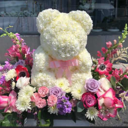 White rose teddy bear surrounded by pink and purple flowers