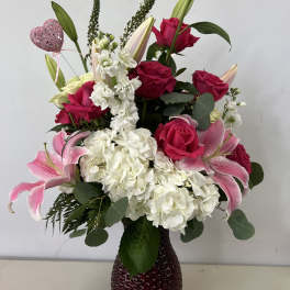 Pink roses and lilies arranged in a dark glass vase with white hydrangeas.