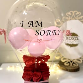 Clear balloon with pink balloons and red roses in a box