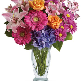 Mixed bouquet of pink lilies, roses, gerbera daisies, and hydrangea in a glass vase