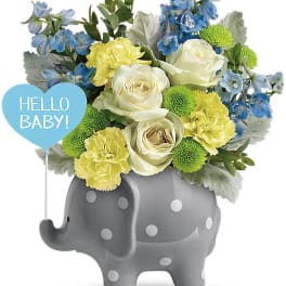 Blue and yellow flower arrangement in a gray elephant planter with a "Hello Baby!" sign