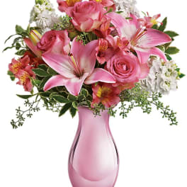 Pink roses and lilies in a pink glass vase with white filler flowers