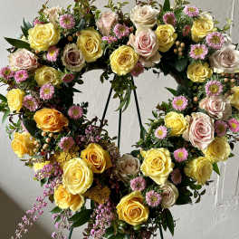 Heart-shaped floral wreath with yellow and blush roses and pink daisies