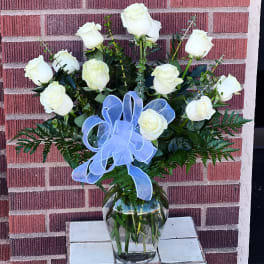 White roses arranged in a clear glass vase with a blue ribbon