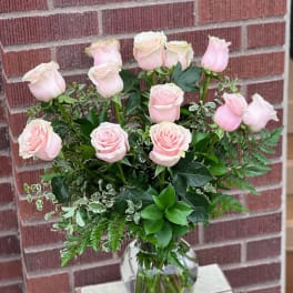 Pink roses arranged in a clear glass vase with mixed greenery