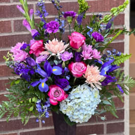 Colorful bouquet in a tall dark vase with roses, hydrangea, and purple blooms