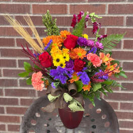 Colorful mixed bouquet in a burgundy vase with a ribbon bow