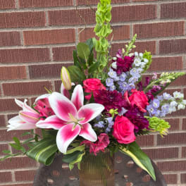 Pink lilies and roses in a glass vase with purple flowers