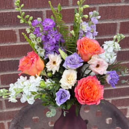 Mixed bouquet of orange roses, purple blooms, and white flowers in a vase