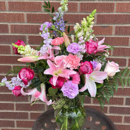 Pink and lavender mixed bouquet with lilies, roses, and carnations in a glass vase