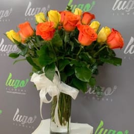 Bouquet of orange and yellow roses in a clear glass vase with a white ribbon