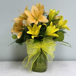 Yellow and peach lilies arranged in a glass vase with a ribbon bow.