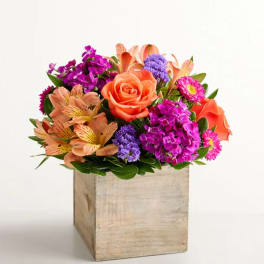 Mixed bouquet of orange, pink, and purple flowers in a wooden box