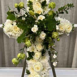 White floral cross on an easel with roses and chrysanthemums