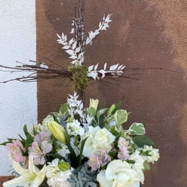 White and pale pink floral arrangement in a wicker basket with a tall cross centerpiece