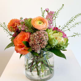 Mixed bouquet of orange, pink, and peach flowers in a clear glass vase