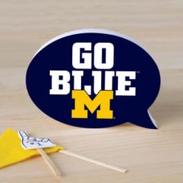 Blue speech bubble sign with "GO BLUE M" text and a small yellow pennant