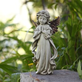 Small angel statue with folded hands on a stone surface