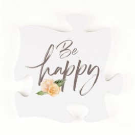 White puzzle piece sign with "Be happy" text and a small floral accent