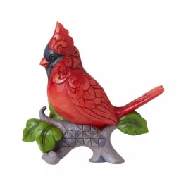 Carved red cardinal figurine perched on a gray base with green leaves