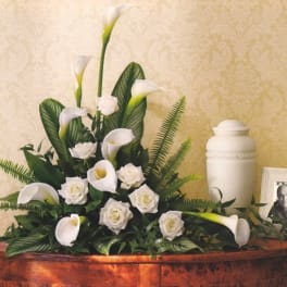 White calla lilies and roses arranged beside an urn and framed photo