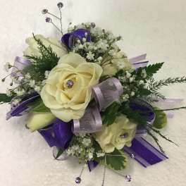 Cream rose corsage with purple ribbon and small white filler flowers