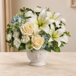 White lilies, cream roses, and blue hydrangeas in a white vase