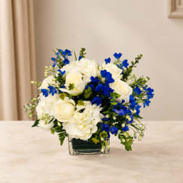 White roses and hydrangeas with blue flowers in a square glass vase