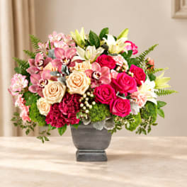 Mixed bouquet of pink roses, lilies, and orchids in a gray vase