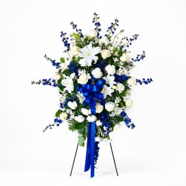 Standing floral spray with white lilies, roses, and blue flowers on a stand