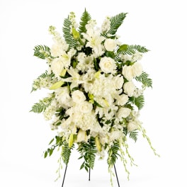 White funeral spray with roses, lilies, and ferns on a stand