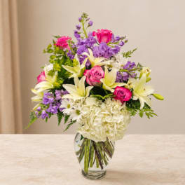 Bouquet of pink roses, white lilies, and purple flowers in a glass vase