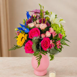 Colorful bouquet of mixed flowers in a pink vase with a small candle nearby