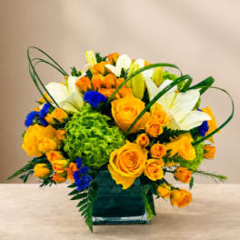 Yellow roses and white lilies in a square glass vase