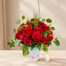 Red roses arranged in a white vase with a small candle beside it