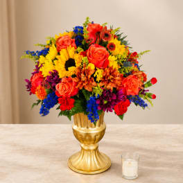 Colorful bouquet of mixed flowers in a gold vase with a candle nearby
